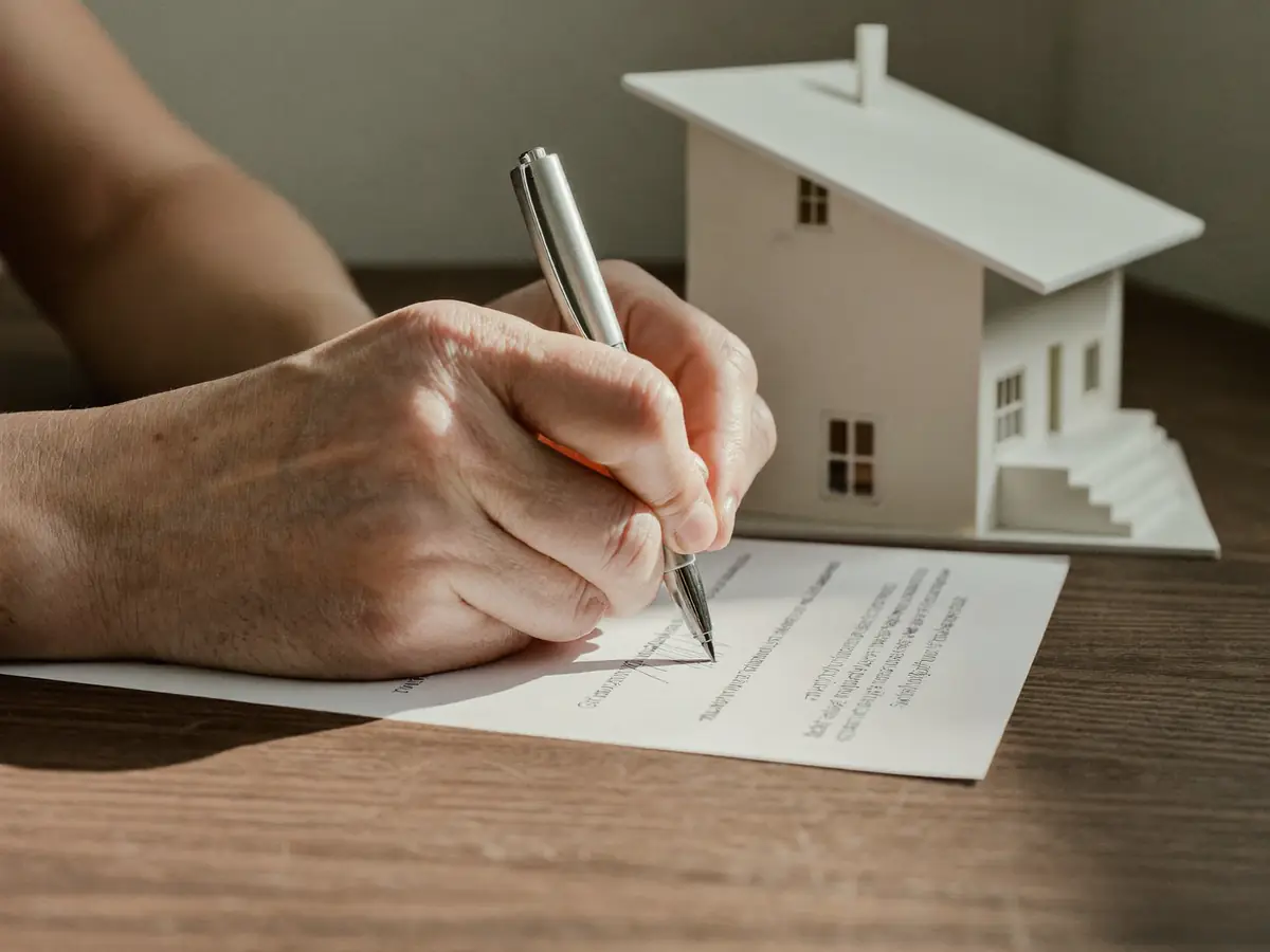 Hands signing a contract next to a small model house