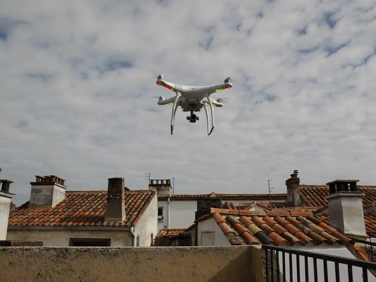 A white inspection drone hovering above old terracotta tiled roofs and chimneys