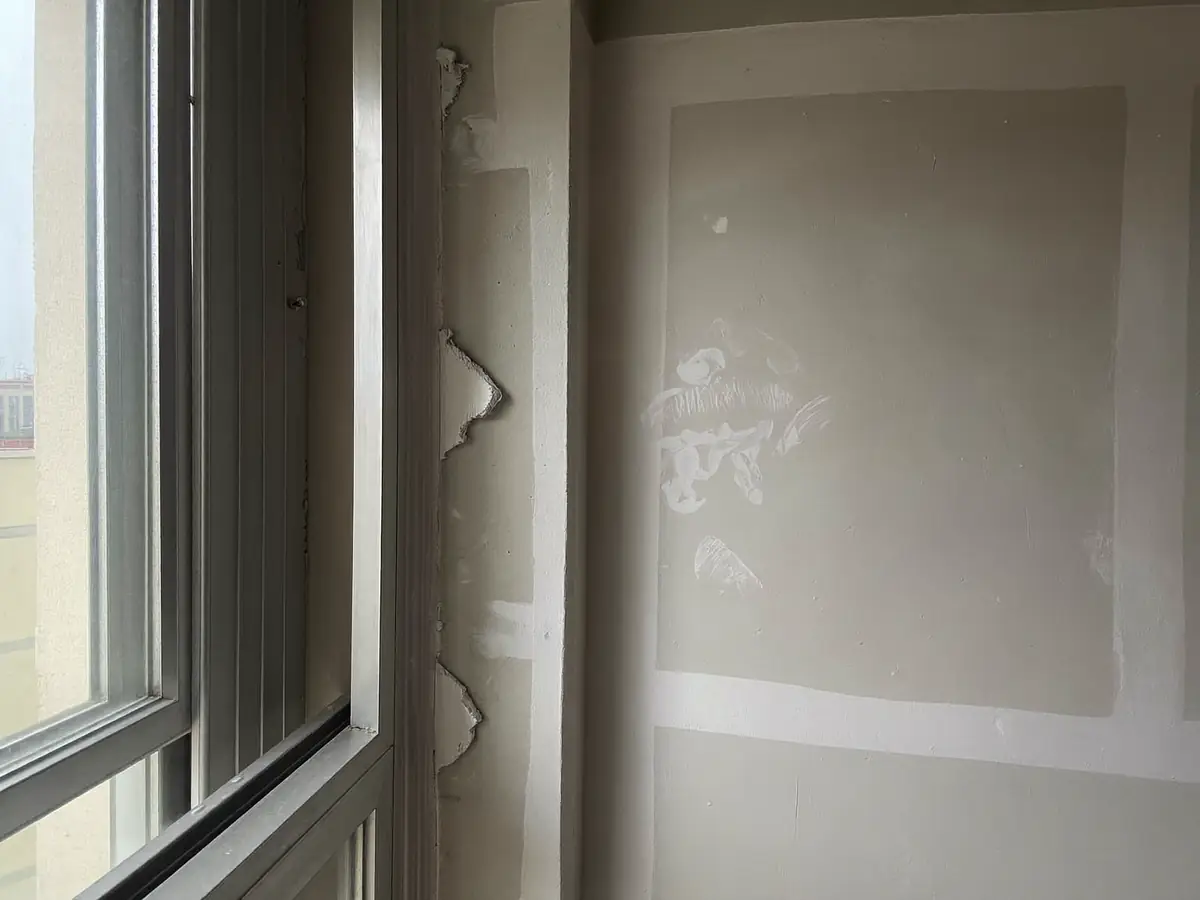 Close-up of a new apartment window frame and wall corner with uneven paint and poor sealant