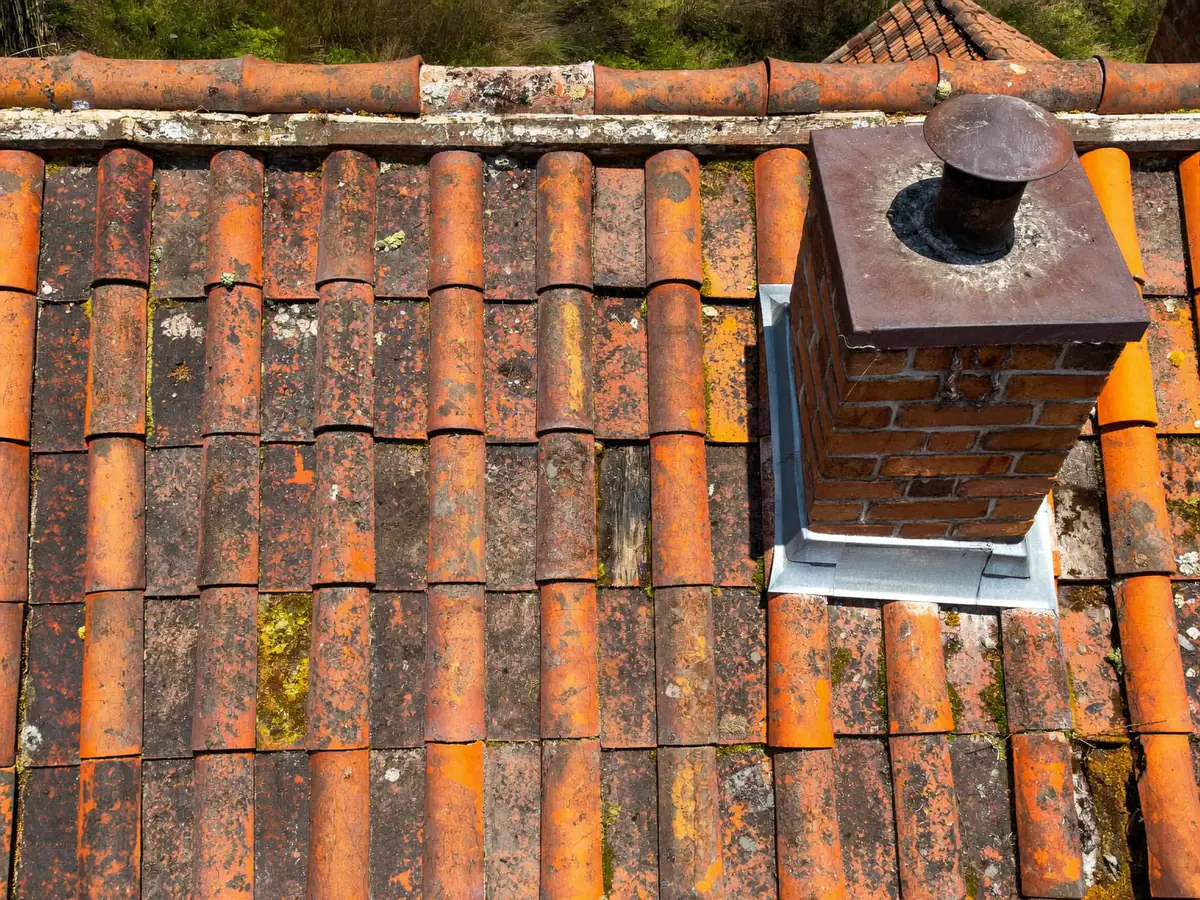 Old terracotta roof tiles with moss and a cracked tile beside a chimney