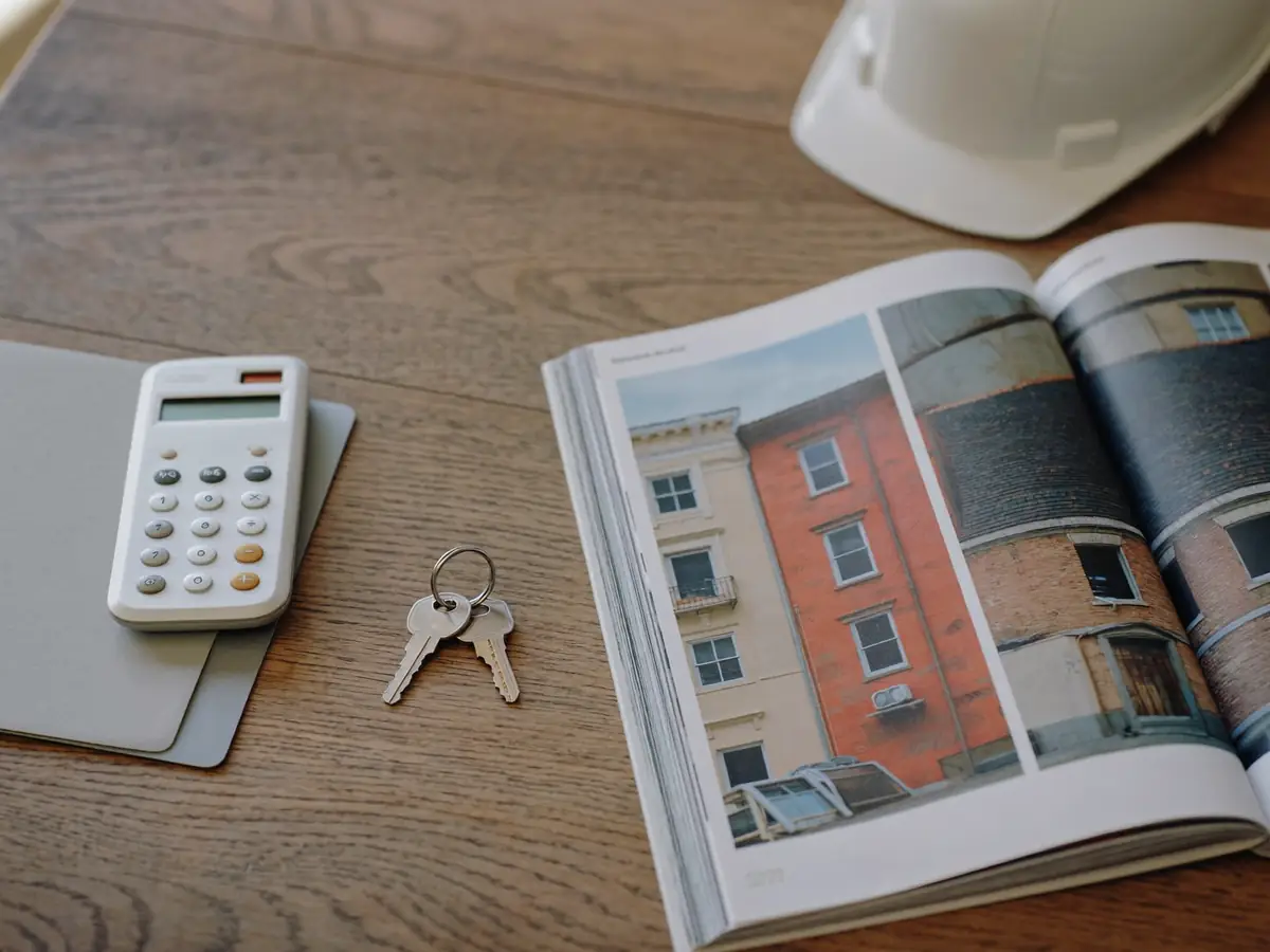 A calculator on a closed folder and a set of apartment keys beside an open photographed inspection report and a hard hat